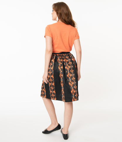 This is the back of a Unique Vintage Halloween swing skirt that has black cats, bats and skulls with orange print and the model is wearing an orange shirt.