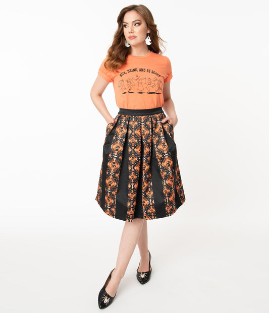 This is a Unique Vintage Halloween swing skirt that has black cats, bats and skulls with orange print and the model is wearing an orange shirt.