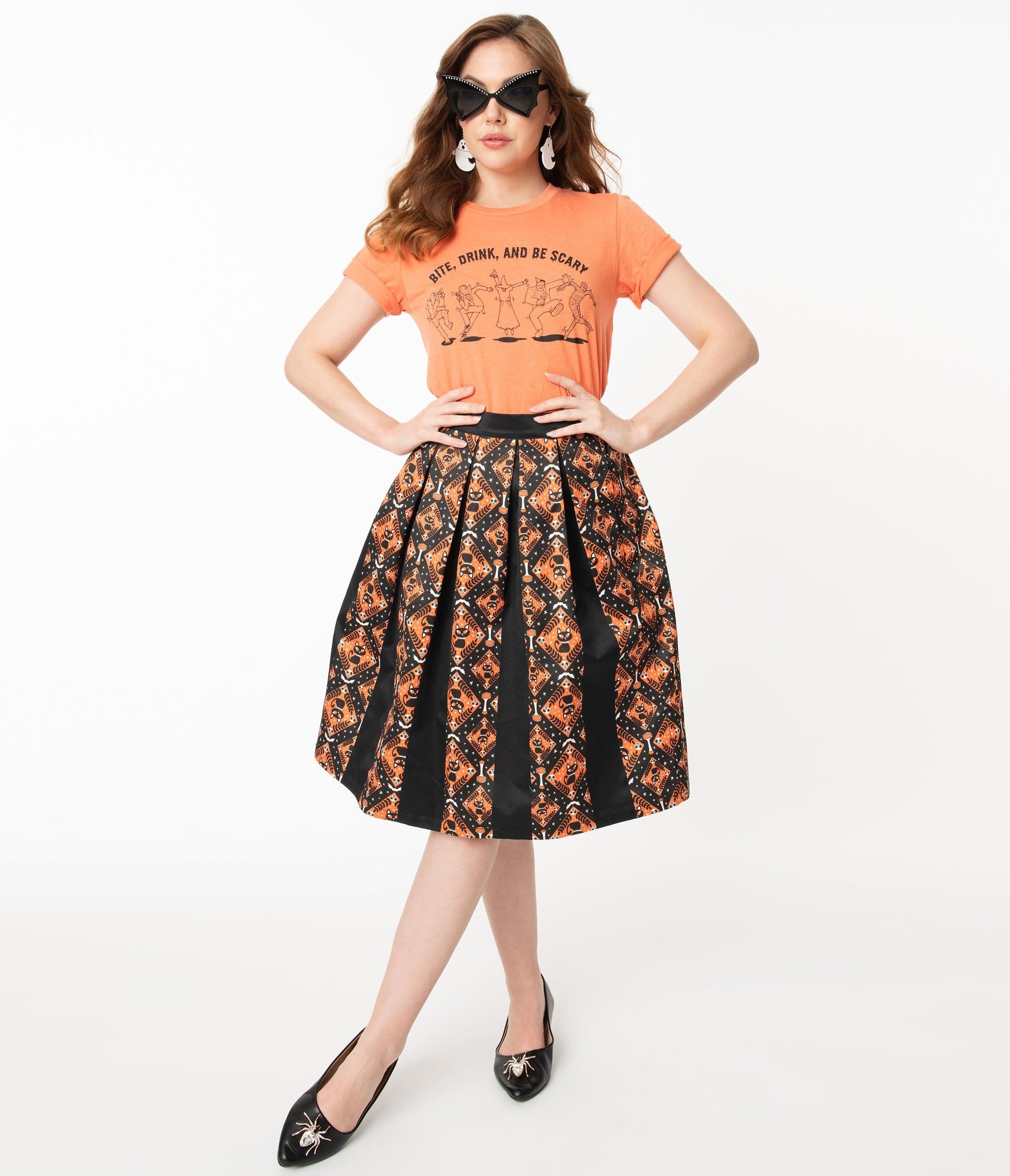 This is a Unique Vintage Halloween swing skirt that has black cats, bats and skulls with orange print and the model is wearing an orange shirt and sunglasses.