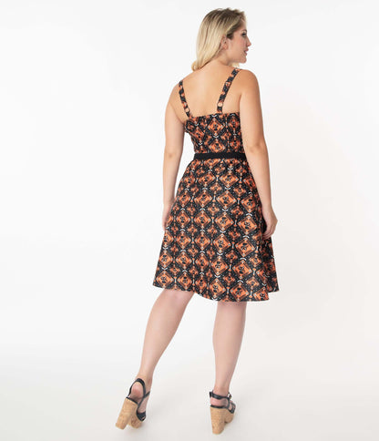 This is a Unique Vintage Halloween Rachel swing dress that has black cats, bats and skulls with orange print, 2 straps and the model is wearing black and cork shoes.